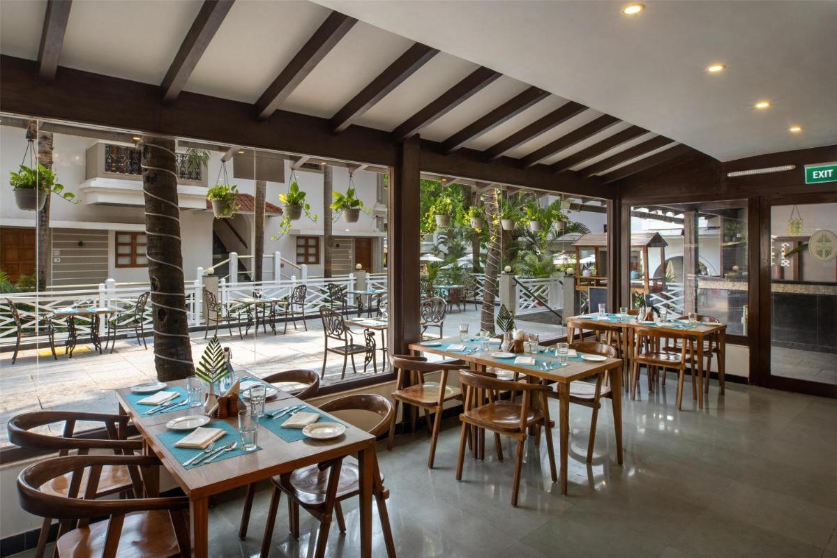 a restaurant with wooden tables and chairs and windows at Radisson Goa Candolim in Candolim