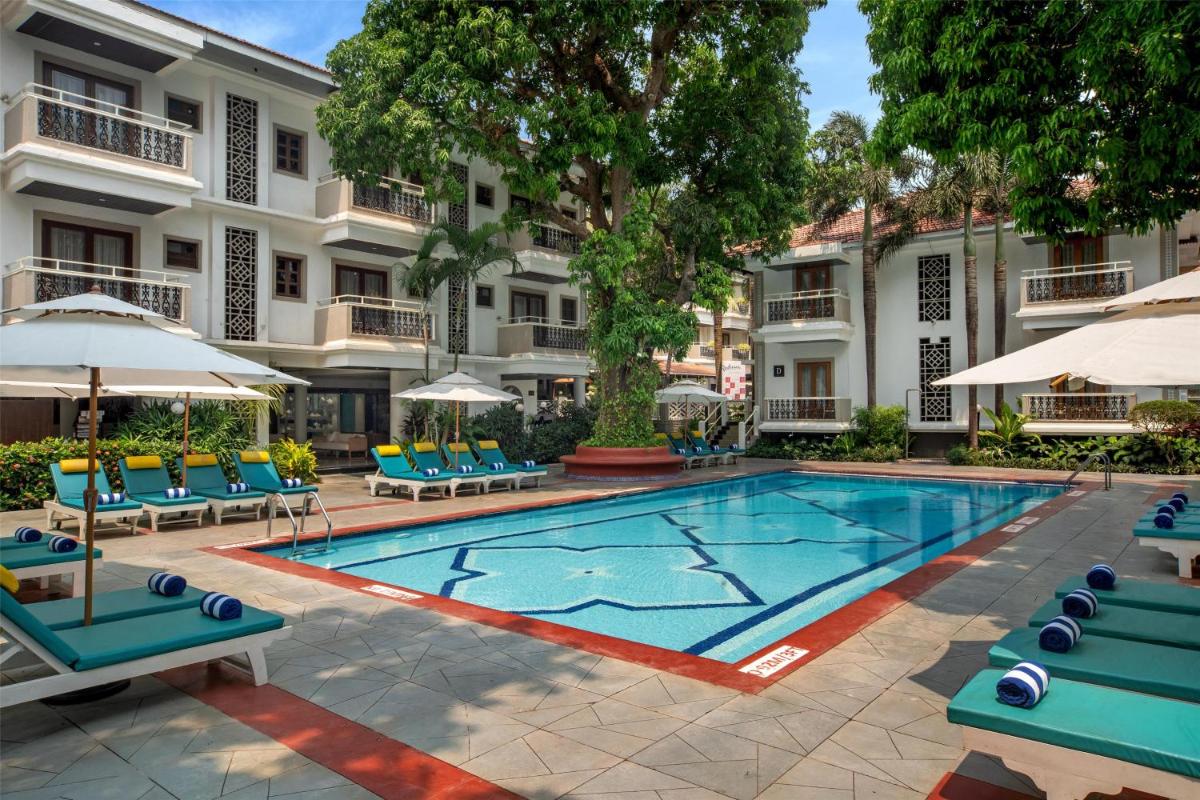 a swimming pool with chairs and umbrellas in front of a building at Radisson Goa Candolim in Candolim