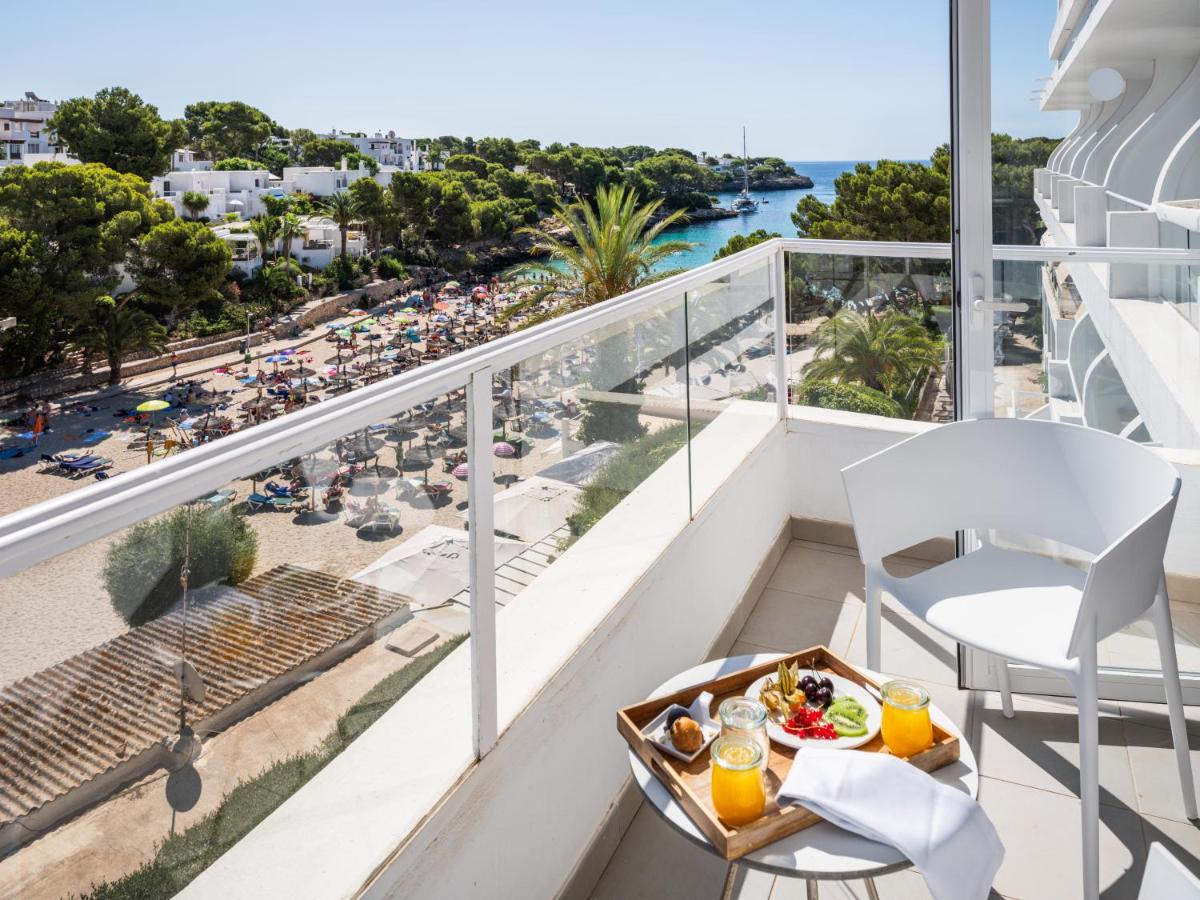 balcón con plato de comida y vistas a la playa en Grupotel Rocador - Adults Only, en Cala d´Or