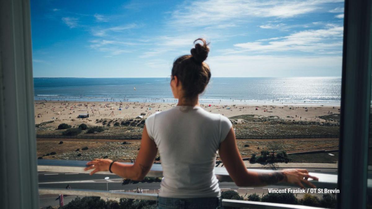 une femme qui regarde par une fenêtre à la plage dans l'établissement Hôtel Spa du Beryl St Brévin l'Océan, à Saint-Brévin-les-Pins