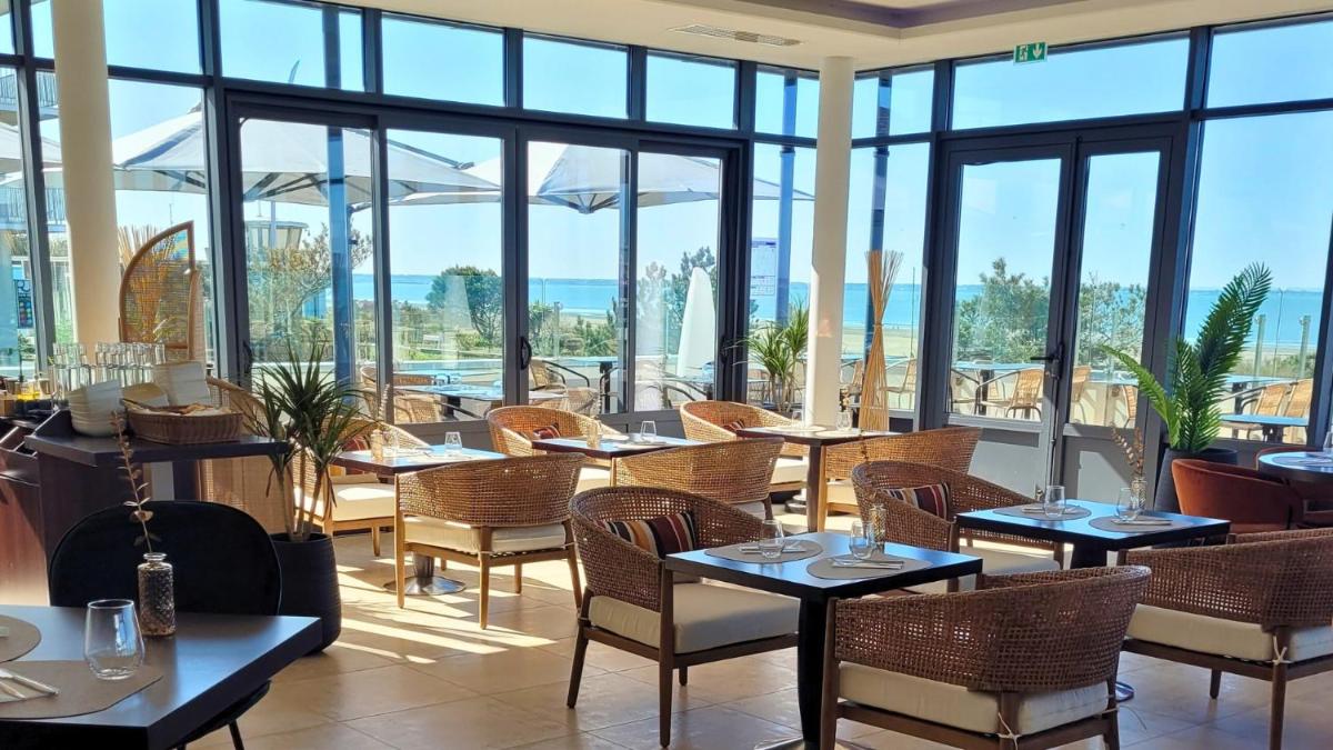 un restaurant avec des tables, des chaises et des fenêtres dans l'établissement Hôtel Spa du Beryl St Brévin l'Océan, à Saint-Brévin-les-Pins