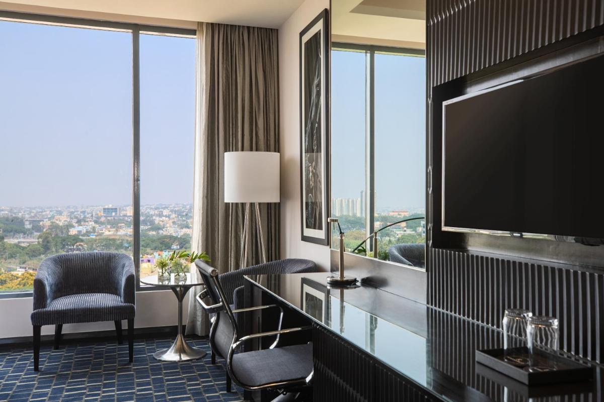 a hotel room with a television and a desk and chairs at Renaissance Bengaluru Race Course Hotel in Bengaluru