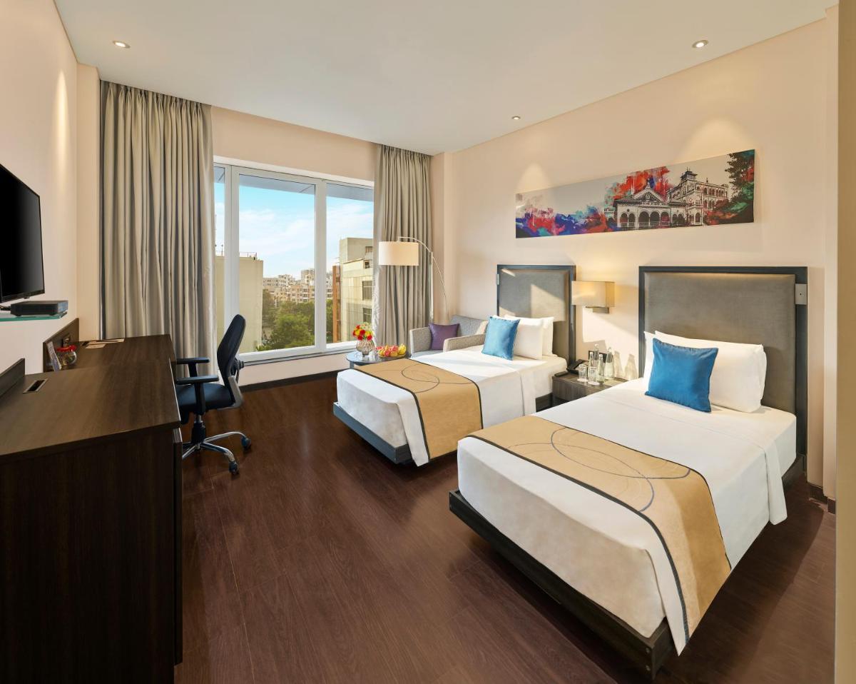 a hotel room with two beds and a desk at Vivanta Pune, Hinjawadi in Pune a hotel room with two beds and a desk at Vivanta Pune, Hinjawadi in Pune