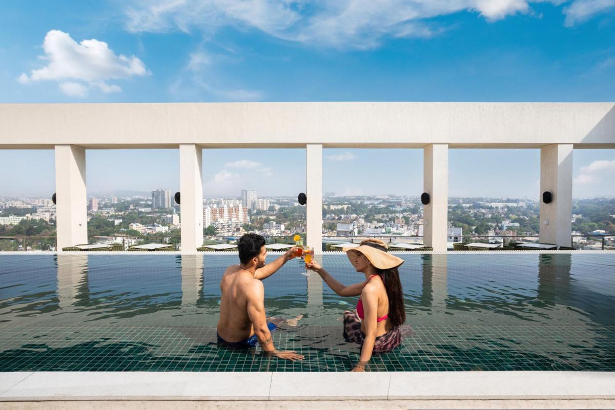 a man and woman sitting on the edge of a swimming pool at DoubleTree by Hilton-Pune Chinchwad in Pune
