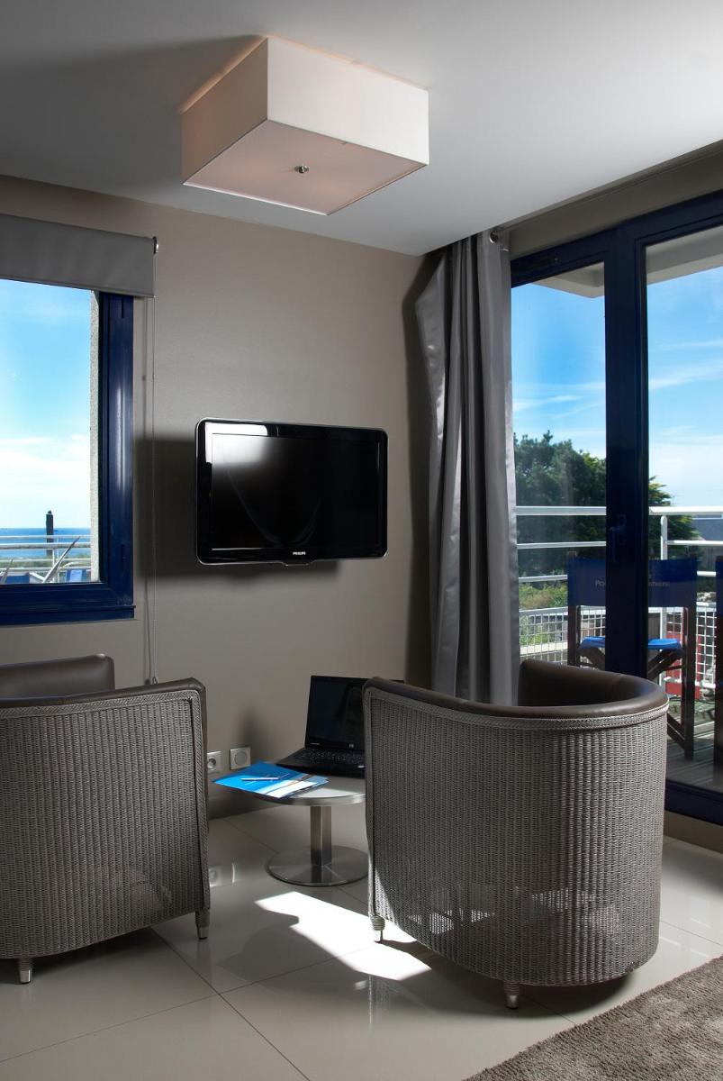 un salon avec deux fauteuils, une télévision et des fenêtres dans l'établissement Hostellerie de la Pointe Saint-Mathieu - SPA & Restaurant, à Plougonvelin