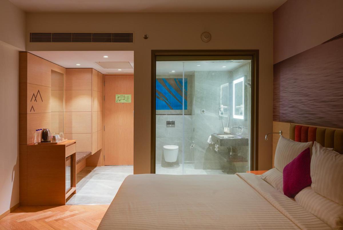 a bedroom with a bed and a bathroom with a shower at Novotel Vijayawada Varun in Vijayawāda