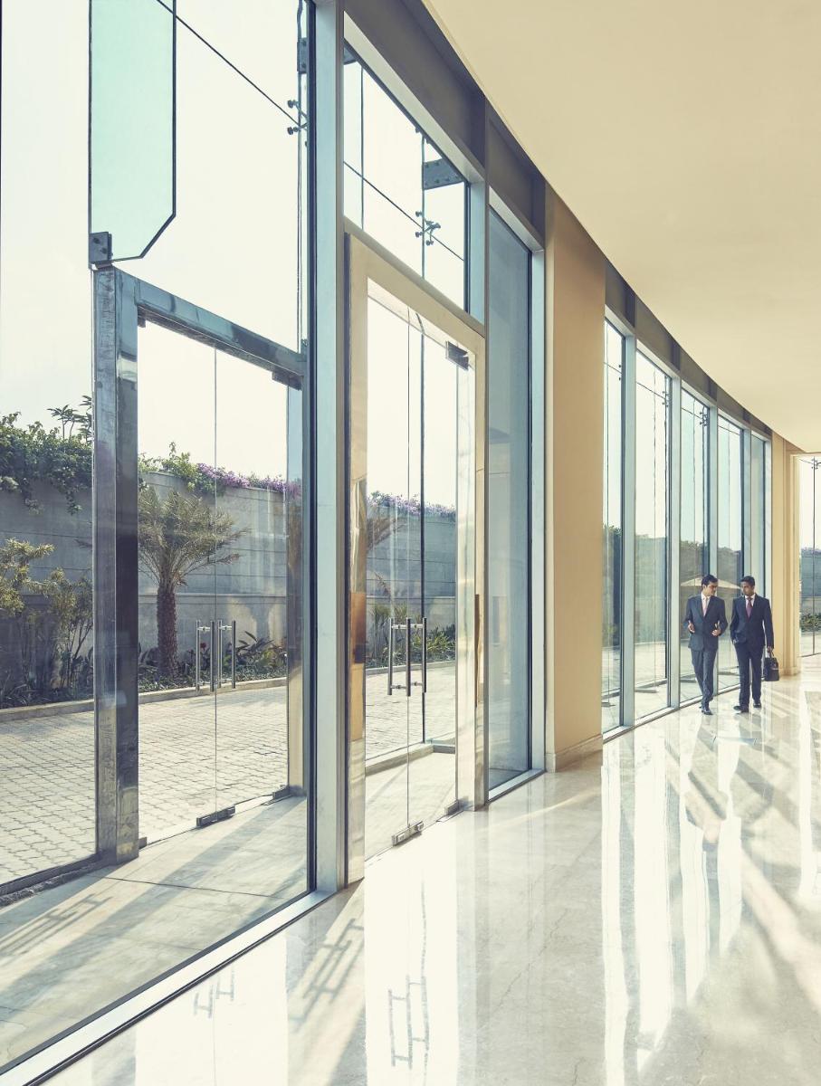 two people walking in a building with large windows at Taj Bangalore in Devanahalli-Bangalore
