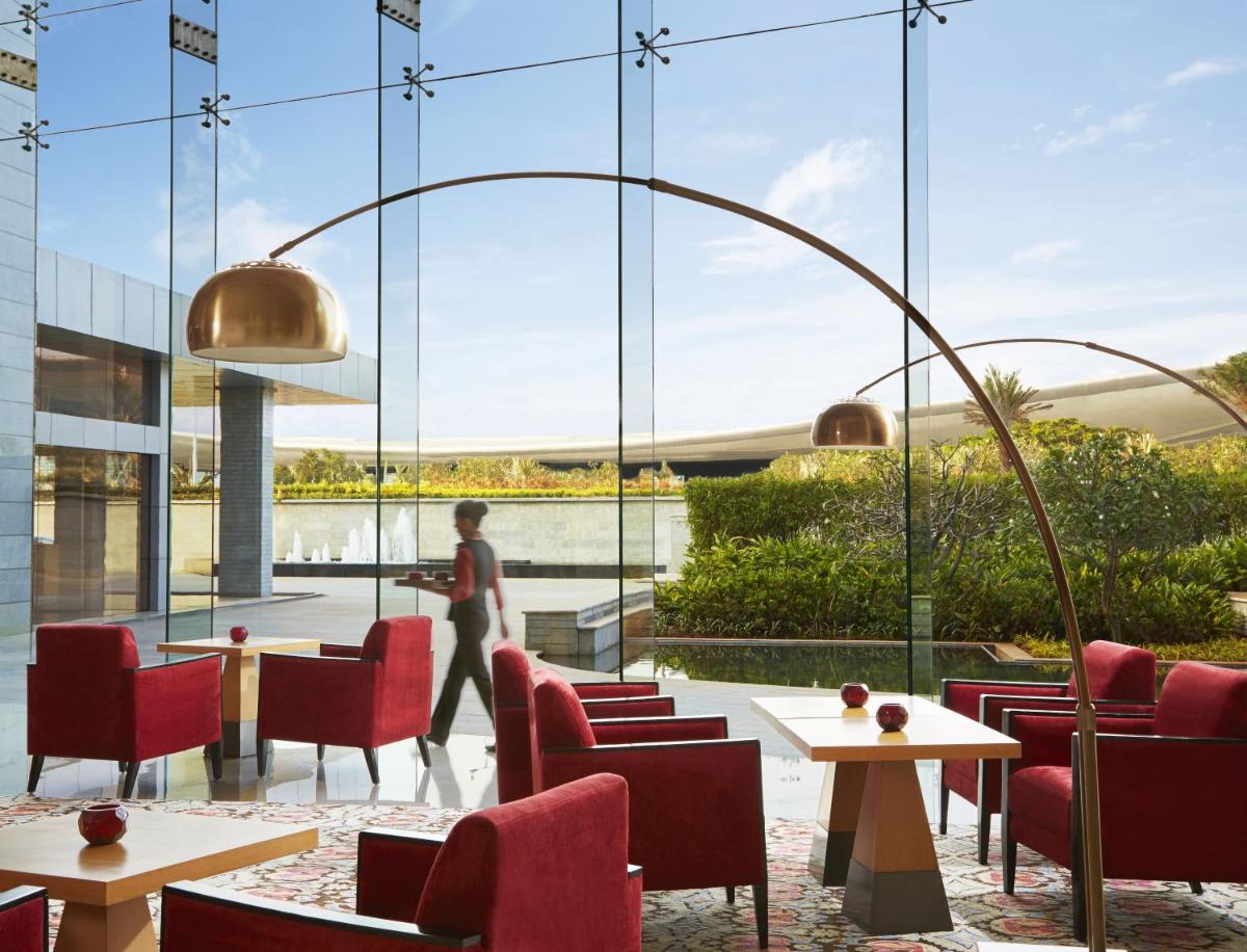 a restaurant with red chairs and tables and a large window at Taj Bangalore in Devanahalli-Bangalore