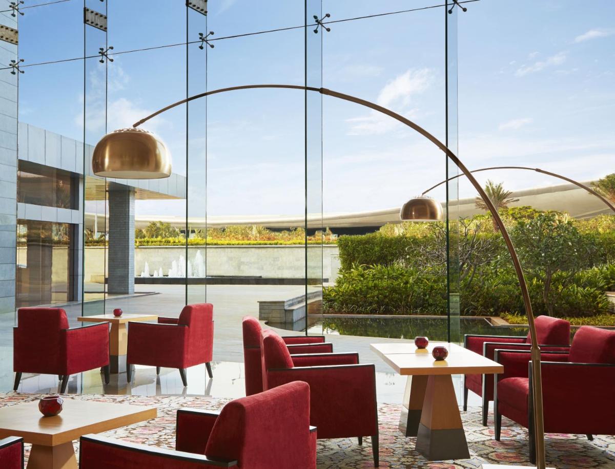 a restaurant with red chairs and tables and a large window at Taj Bangalore in Devanahalli-Bangalore