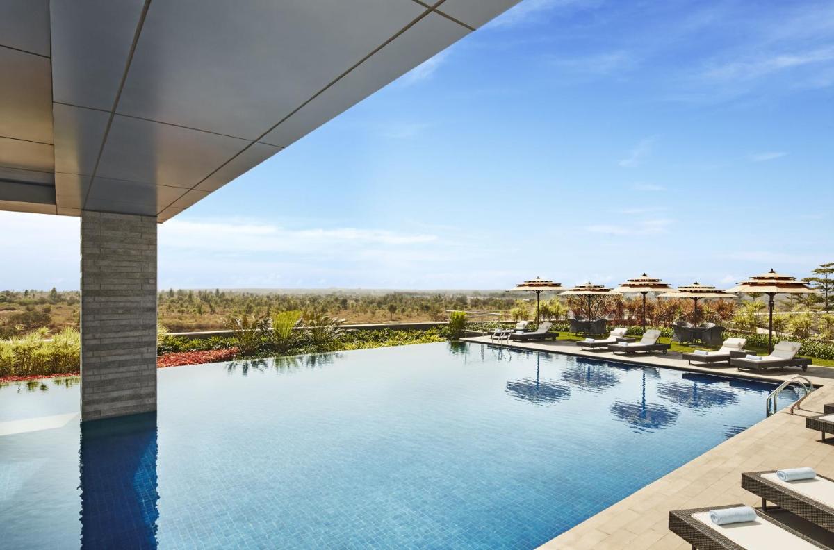 an infinity pool at a resort with chairs and umbrellas at Taj Bangalore in Devanahalli-Bangalore