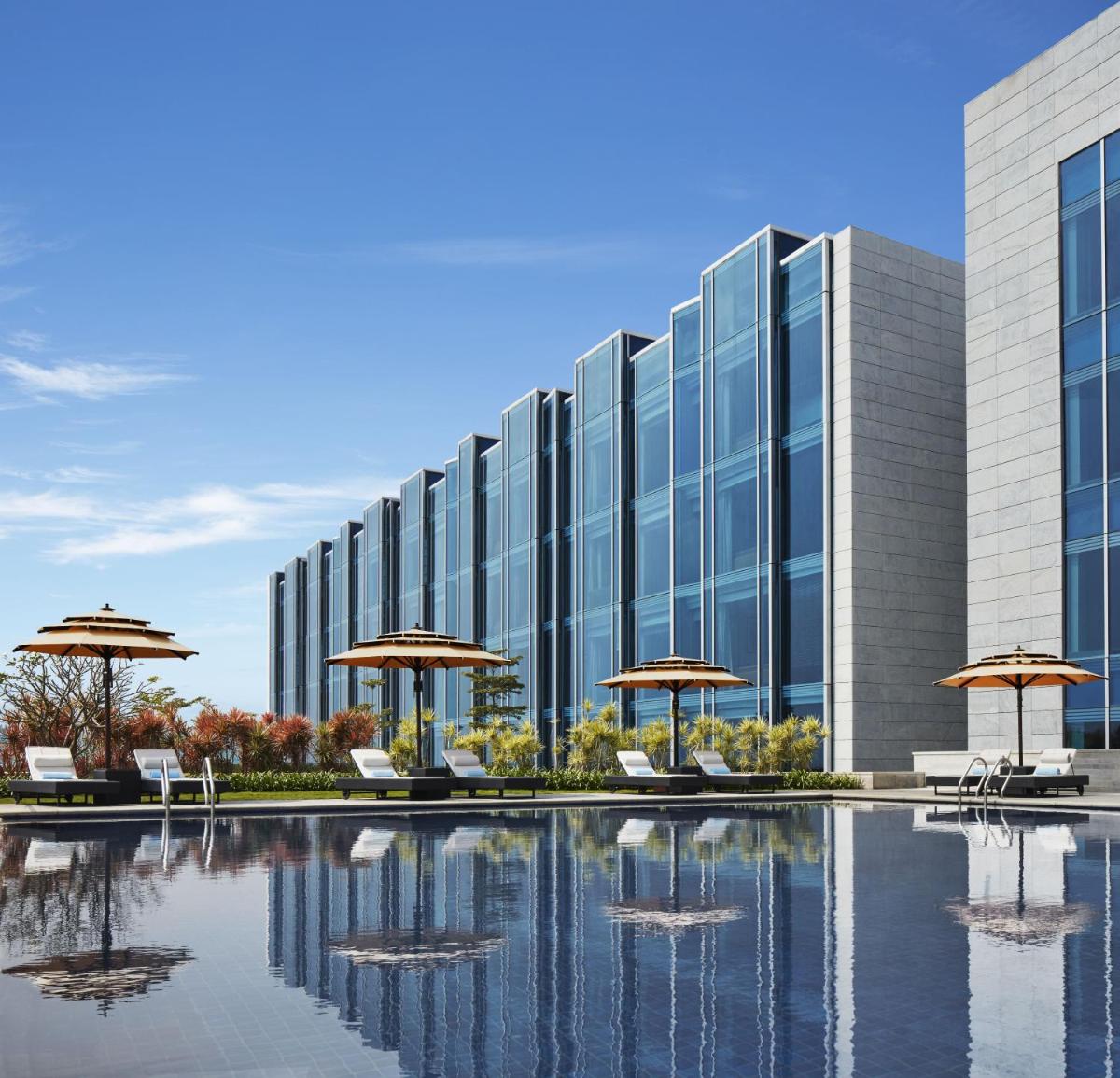 a building with chairs and umbrellas and a pool at Taj Bangalore in Devanahalli-Bangalore