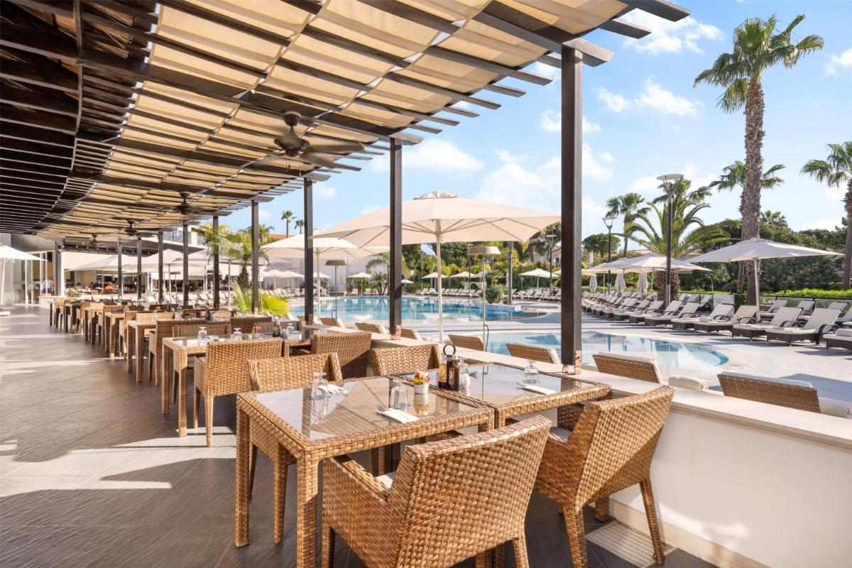 um restaurante com mesas e cadeiras ao lado de uma piscina em Wyndham Grand Algarve na Quinta do Lago