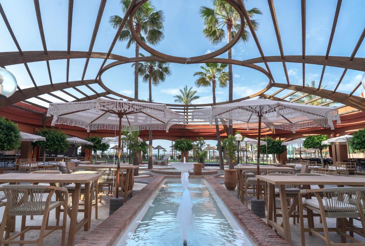 Un restaurante con mesas y sillas y palmeras. en Holiday Premium Resort, en Benalmádena