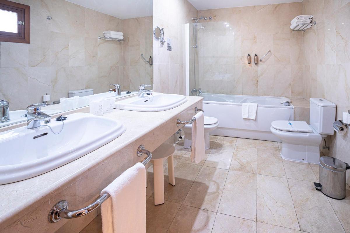Un baño con dos lavabos, una bañera y un inodoro. en Hotel Hurdes Reales, en Las Mestas