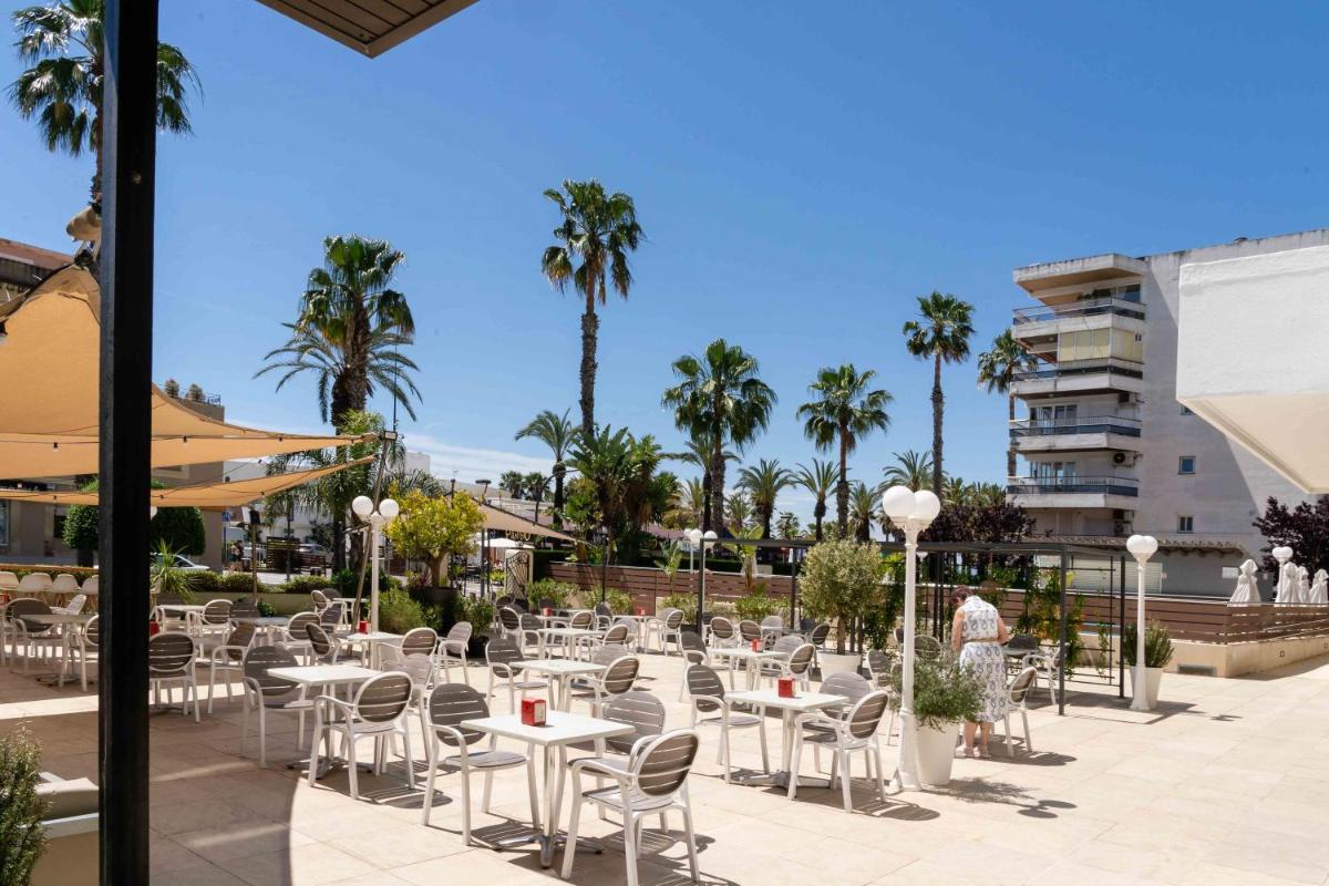 Un patio con mesas y sillas y palmeras. en Hotel Planas, en Salou