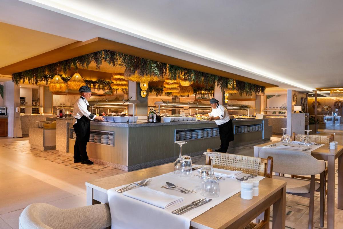 Un restaurante con dos chefs preparando comida en la cocina. en Hotel Riu Palace La Mola, en Playa de Migjorn 112 fotos más