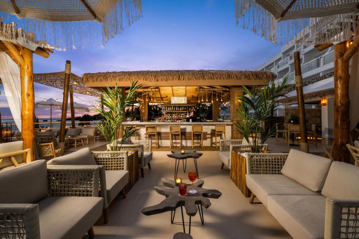 Un restaurante con sofás y un bar en la playa. en Hotel Riu Palace La Mola, en Playa de Migjorn