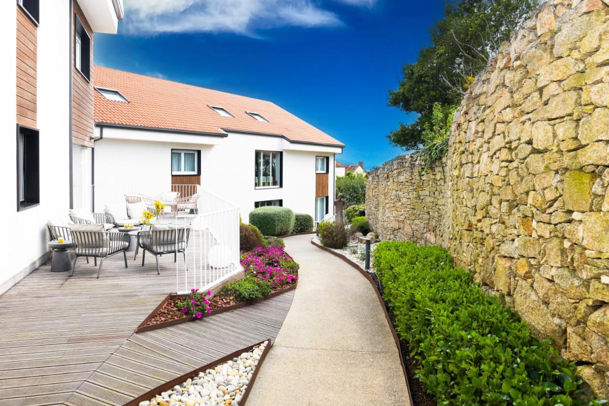 un patio con mesa y sillas junto a una pared de piedra en Hotel Spa Meiga do Mar, en Carnota