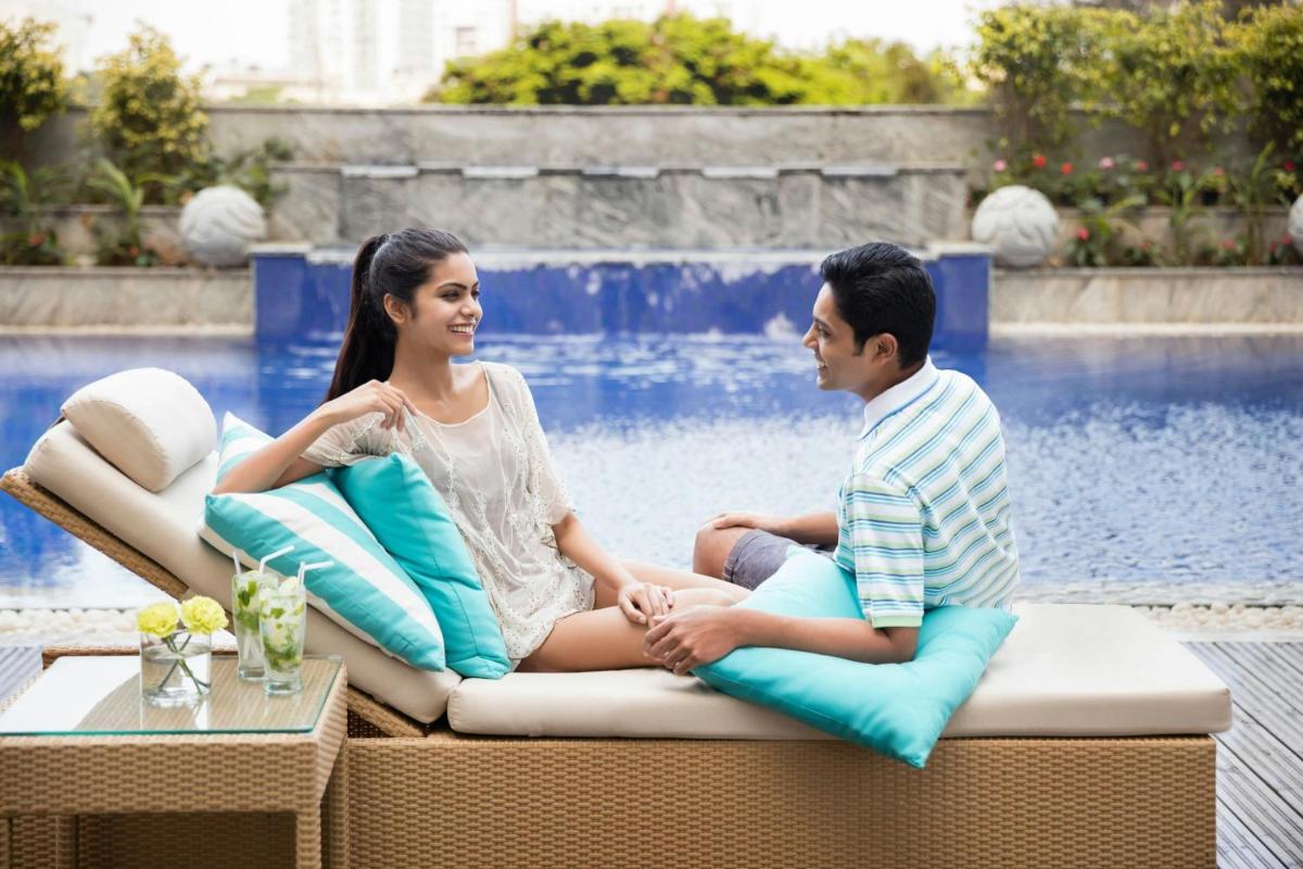 a man and woman sitting on a couch in front of a pool at Courtyard by Marriott Bengaluru Outer Ring Road in Bengaluru