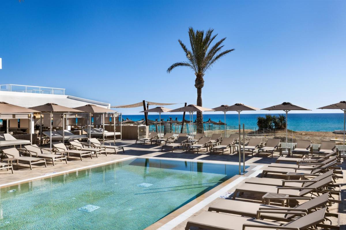 una piscina con tumbonas, una palmera y el océano en Hotel Riu Palace La Mola, en Playa de Migjorn