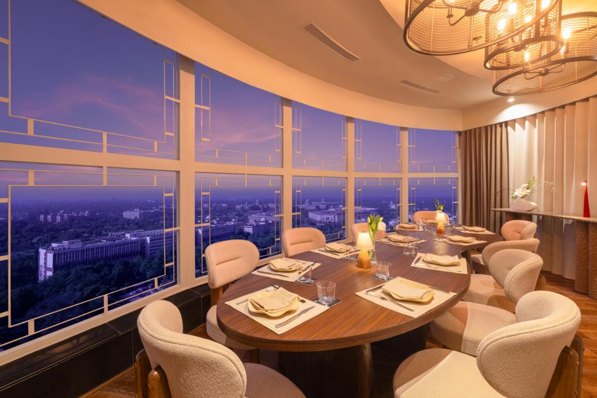 a dining room with a table and chairs and large windows at Le Meridien New Delhi in New Delhi a dining room with a table and chairs and large windows at Le Meridien New Delhi in New Delhi