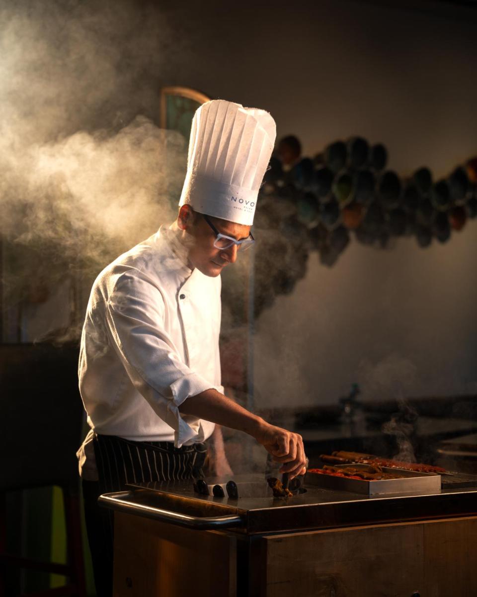 a chef preparing food on top of a grill at Novotel Kolkata Hotel and Residences in Kolkata a chef preparing food on top of a grill at Novotel Kolkata Hotel and Residences in Kolkata