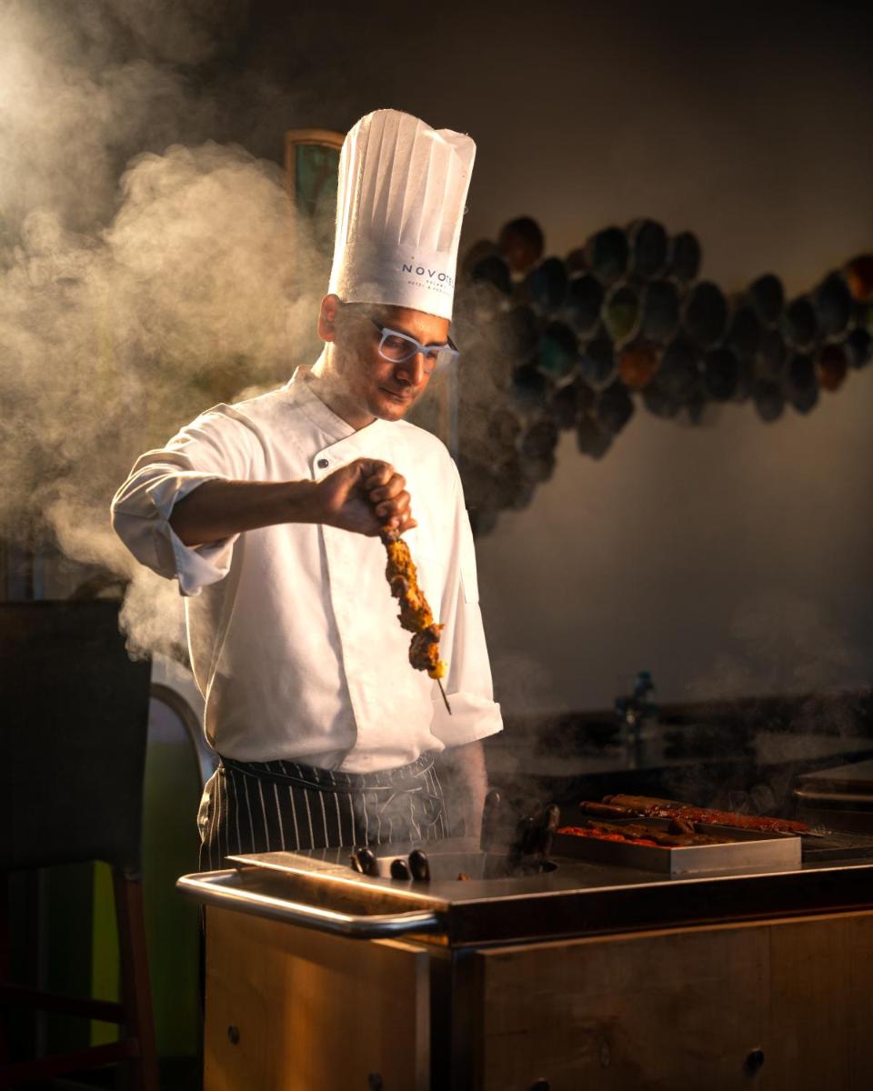 a man in a chefs hat cooking food on a grill at Novotel Kolkata Hotel and Residences in Kolkata a man in a chefs hat cooking food on a grill at Novotel Kolkata Hotel and Residences in Kolkata