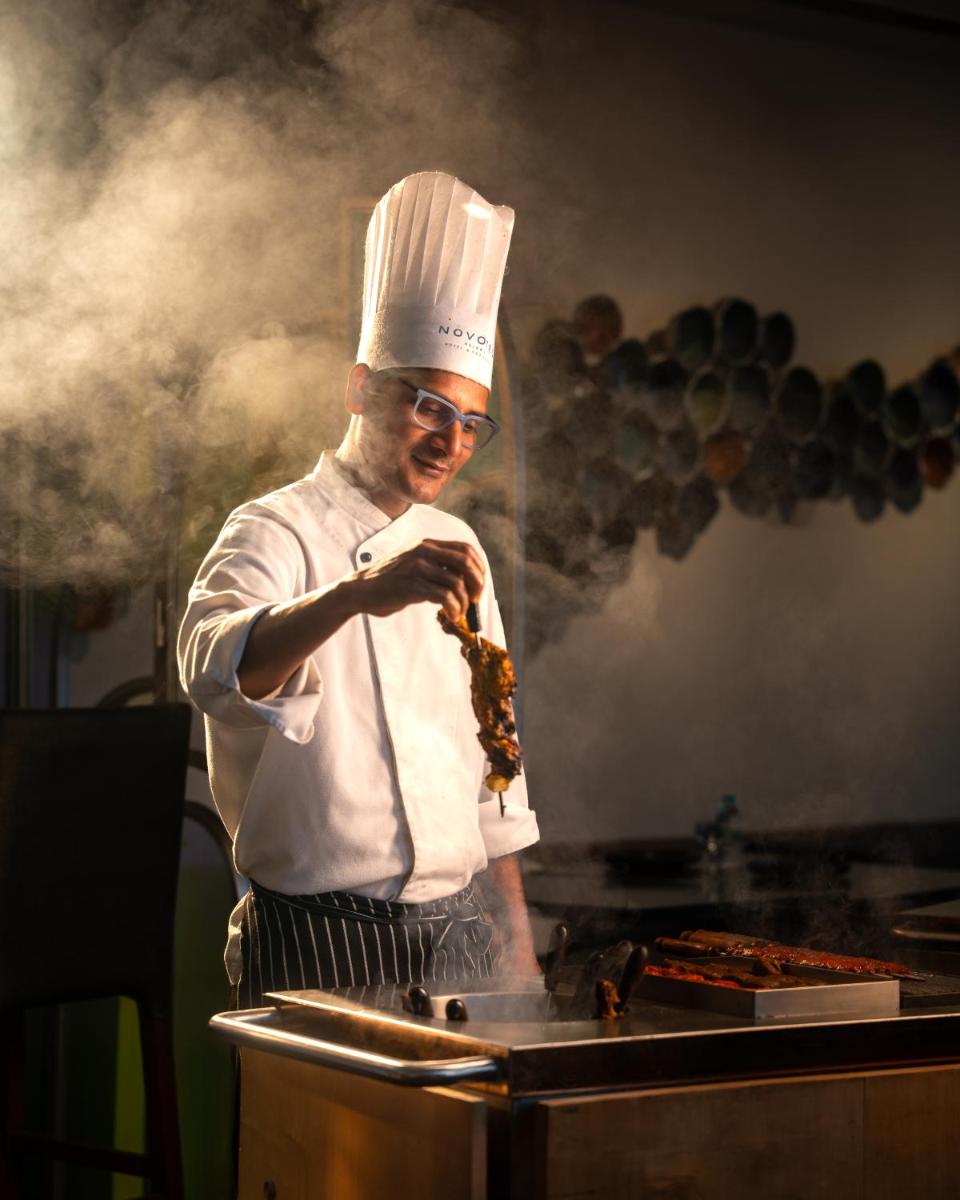a man in a chefs hat preparing food on a grill at Novotel Kolkata Hotel and Residences in Kolkata a man in a chefs hat preparing food on a grill at Novotel Kolkata Hotel and Residences in Kolkata