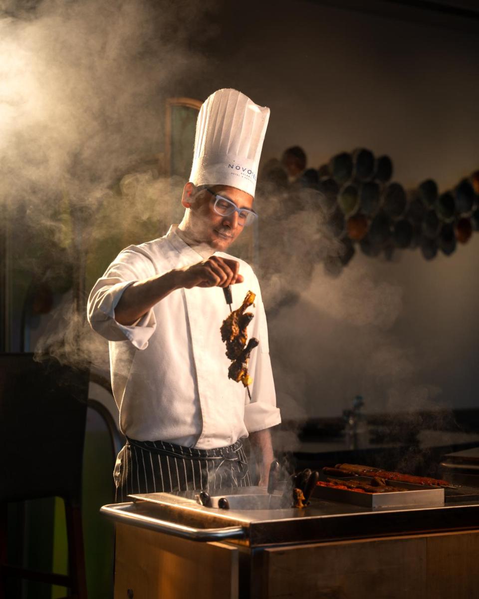 a man in a chefs hat cooking food in a pan at Novotel Kolkata Hotel and Residences in Kolkata a man in a chefs hat cooking food in a pan at Novotel Kolkata Hotel and Residences in Kolkata