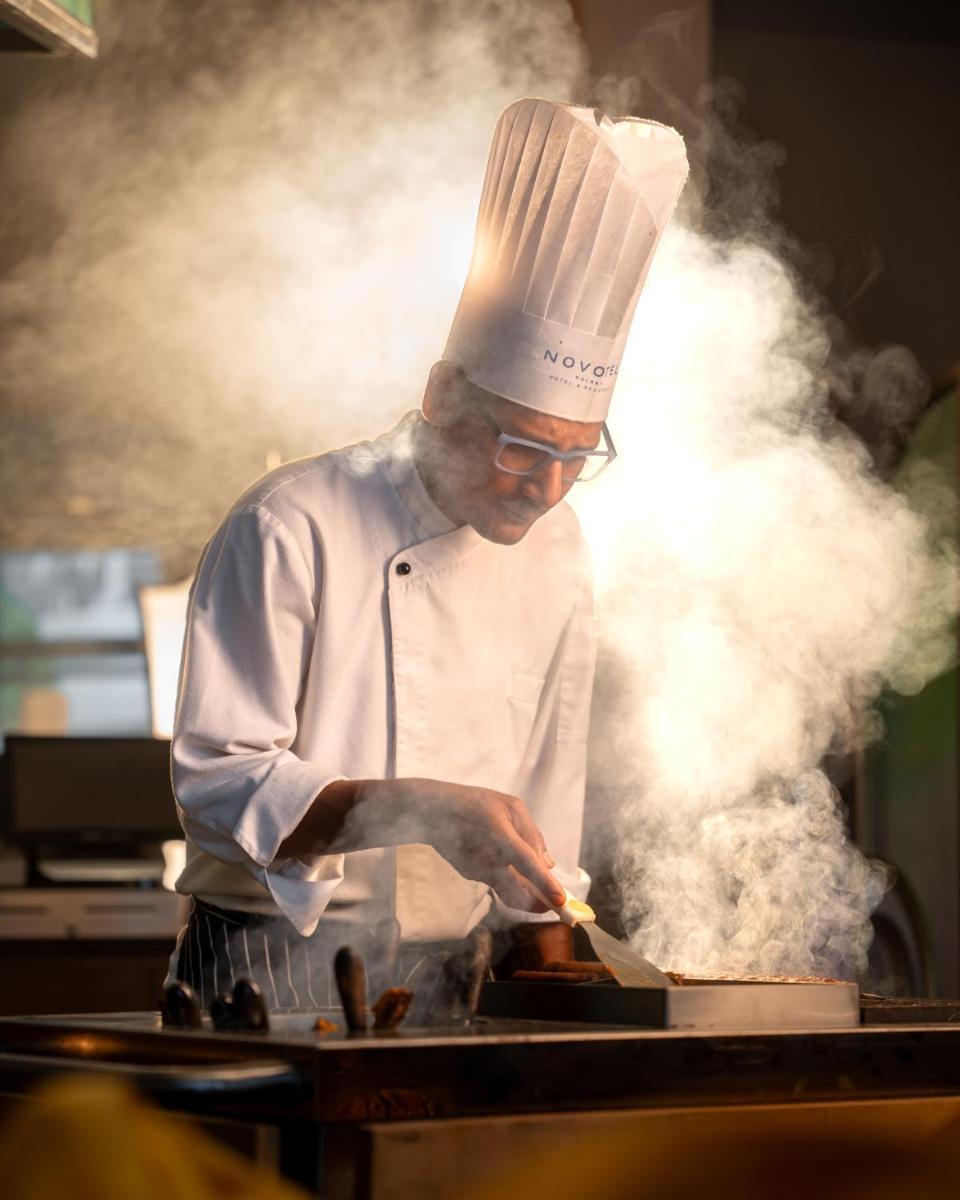 a chef preparing food on top of a grill at Novotel Kolkata Hotel and Residences in Kolkata a chef preparing food on top of a grill at Novotel Kolkata Hotel and Residences in Kolkata