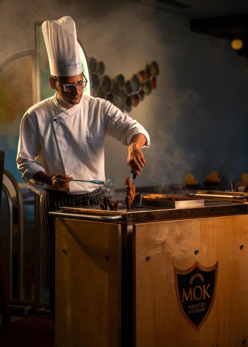 a man in a chefs hat preparing food on a grill at Novotel Kolkata Hotel and Residences in Kolkata a man in a chefs hat preparing food on a grill at Novotel Kolkata Hotel and Residences in Kolkata