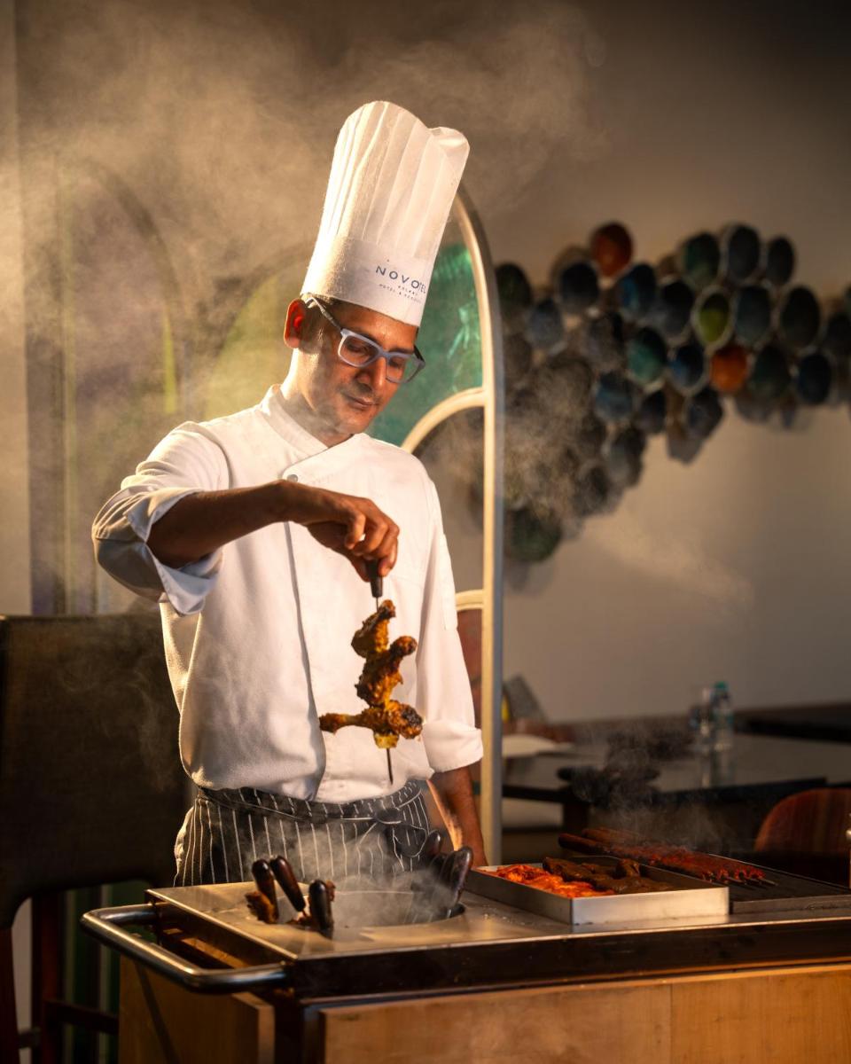 a man in a chefs hat preparing food in a kitchen at Novotel Kolkata Hotel and Residences in Kolkata a man in a chefs hat preparing food in a kitchen at Novotel Kolkata Hotel and Residences in Kolkata