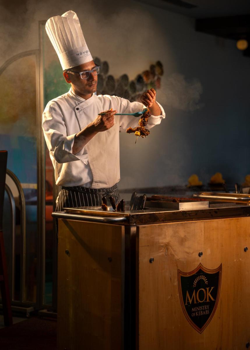 a man in a chefs hat preparing food on a counter at Novotel Kolkata Hotel and Residences in Kolkata a man in a chefs hat preparing food on a counter at Novotel Kolkata Hotel and Residences in Kolkata