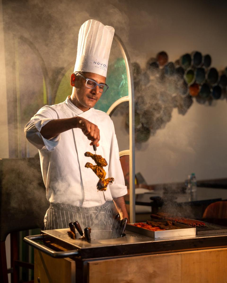 a man in a chefs hat preparing food on a grill at Novotel Kolkata Hotel and Residences in Kolkata a man in a chefs hat preparing food on a grill at Novotel Kolkata Hotel and Residences in Kolkata