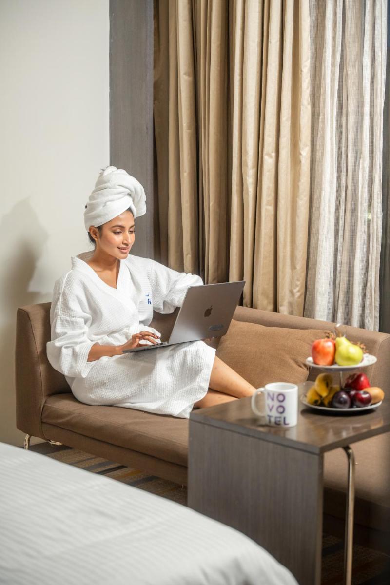 a woman sitting on a couch with a laptop at Novotel Kolkata Hotel and Residences in Kolkata a woman sitting on a couch with a laptop at Novotel Kolkata Hotel and Residences in Kolkata