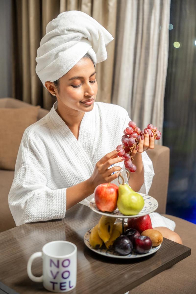 a woman sitting at a table with a plate of fruit at Novotel Kolkata Hotel and Residences in Kolkata a woman sitting at a table with a plate of fruit at Novotel Kolkata Hotel and Residences in Kolkata