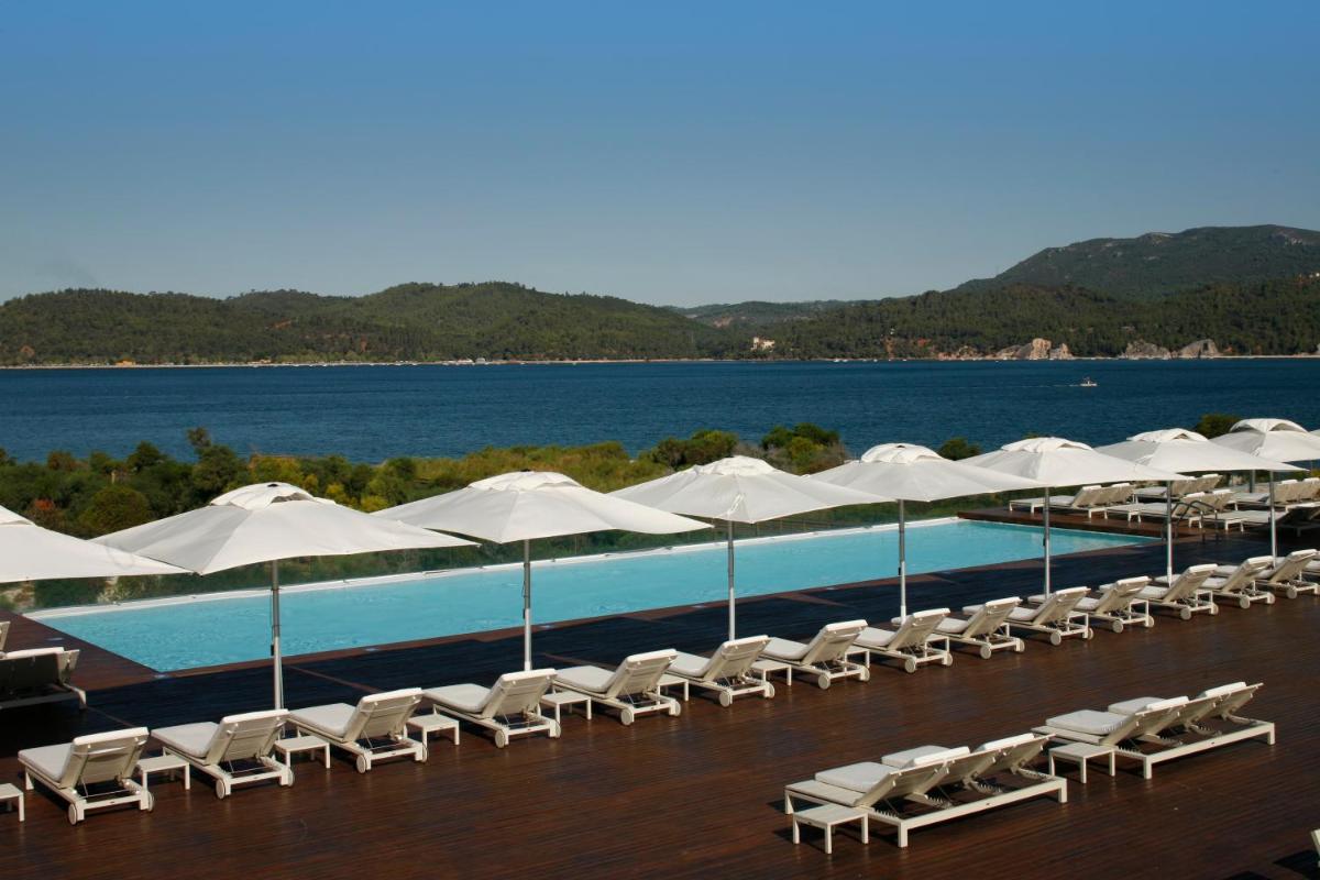 uma piscina com guarda-sóis e cadeiras brancas e a água em Troia Design Hotel em Tróia