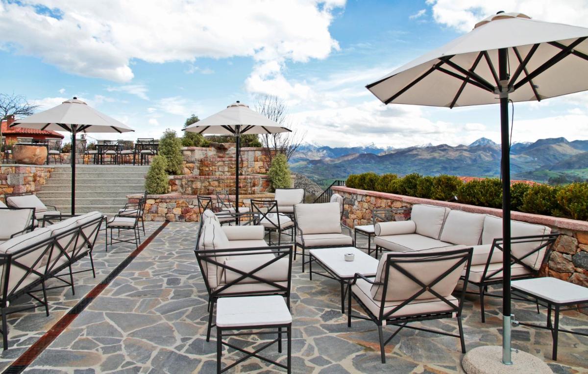 Un patio con sillas, mesas y sombrillas. en Puebloastur Eco Resort Hotel & Spa, en Cofiño