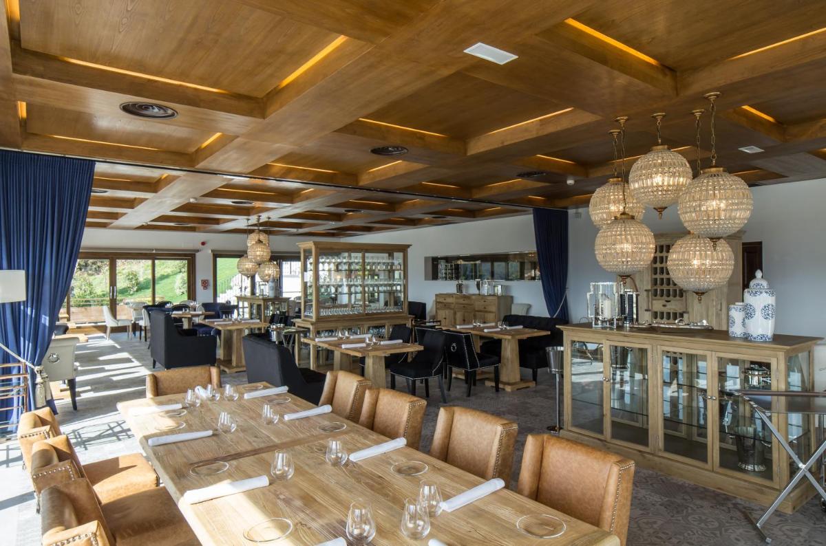 Un restaurante con techos de madera y mesas y sillas. en Puebloastur Eco Resort Hotel & Spa, en Cofiño