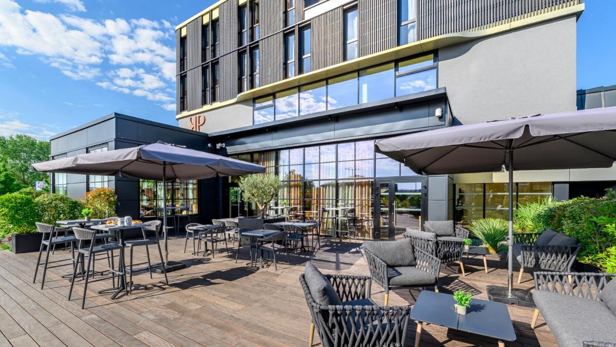 une terrasse avec des tables et des parasols devant un bâtiment dans l'établissement Kyriad Prestige Compiègne Hotel & Spa, à Compiègne