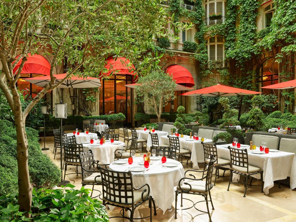 un restaurant avec des tables et des chaises blanches en face d'un bâtiment dans l'établissement Hôtel Plaza Athénée - Dorchester Collection, à Paris