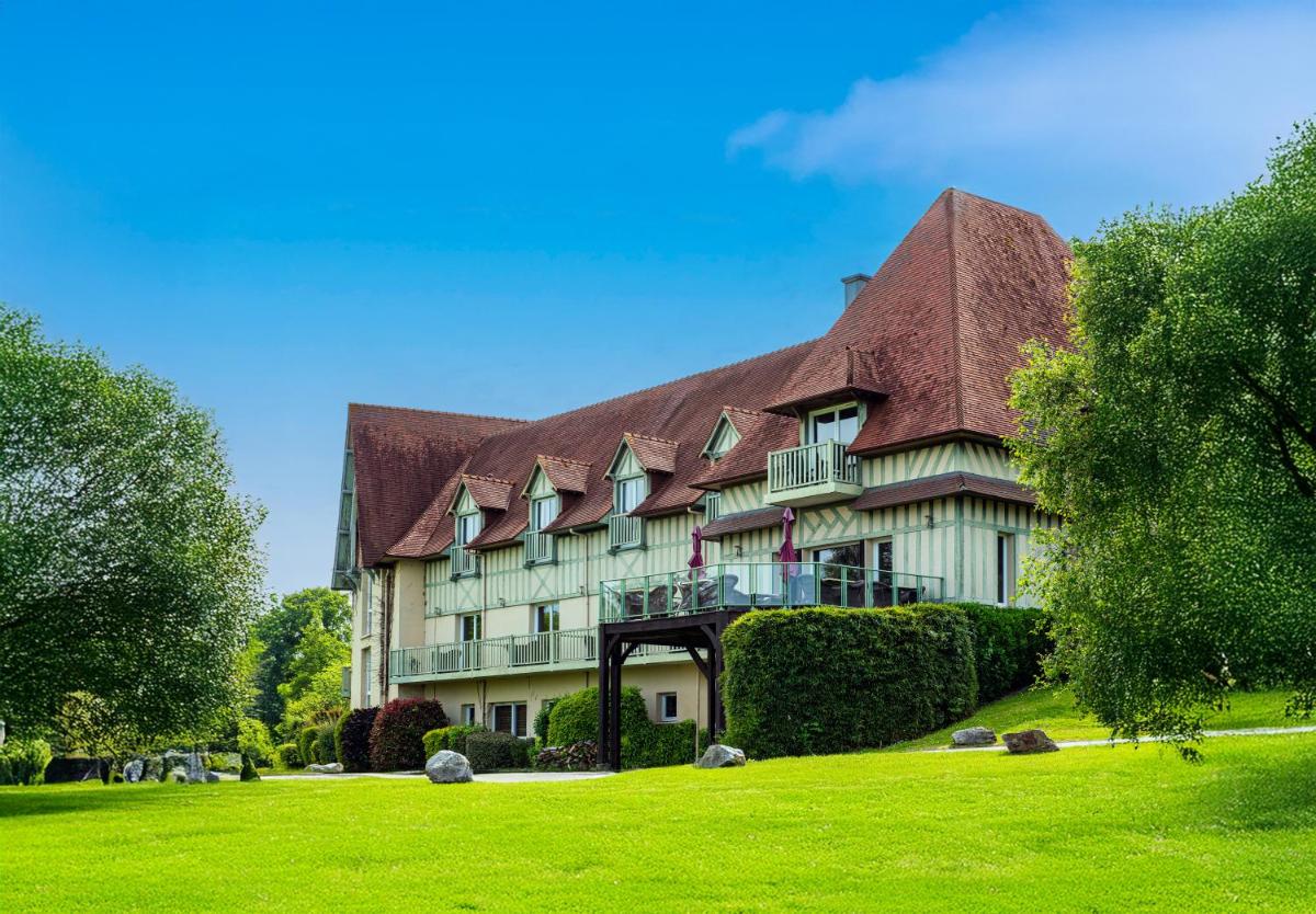 un grand bâtiment avec un toit de chaume sur un champ vert dans l'établissement Domaine De Villers & Spa, à Villers-sur-Mer