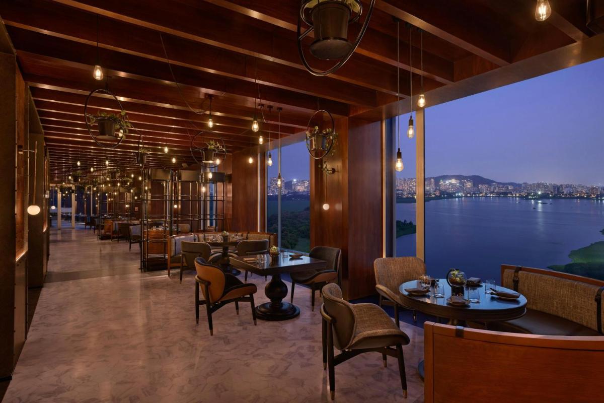 a restaurant with tables and chairs and a view of the water at The Westin Mumbai Powai Lake in Mumbai