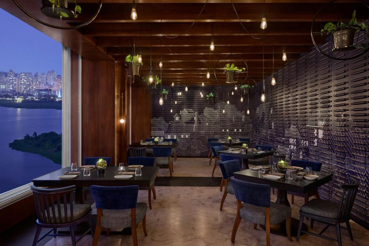 a restaurant with tables and chairs and a large window at The Westin Mumbai Powai Lake in Mumbai