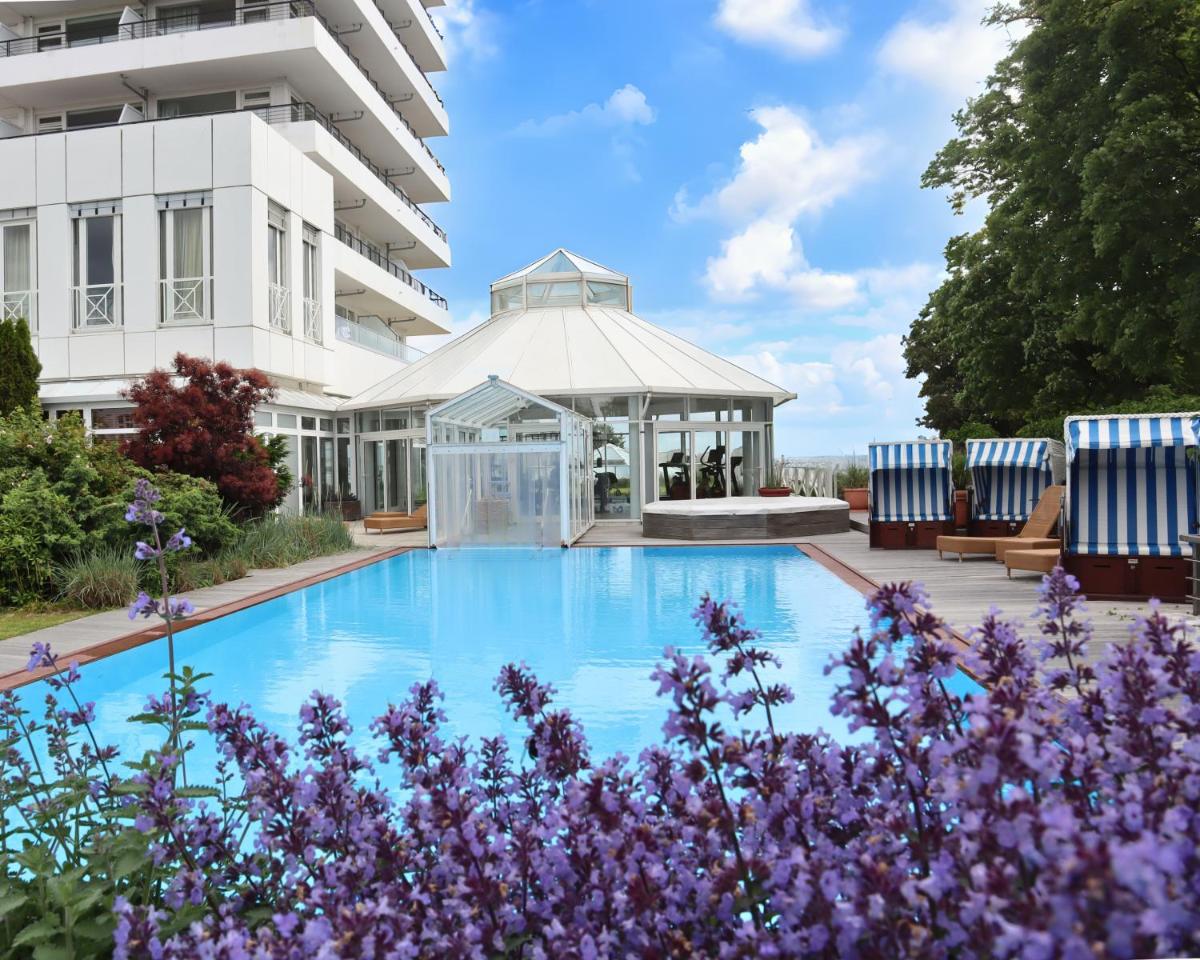 einem Pool vor einem Gebäude mit lila Blumen in der Unterkunft Grand Hotel Seeschlösschen Sea Retreat & SPA in Timmendorfer Strand