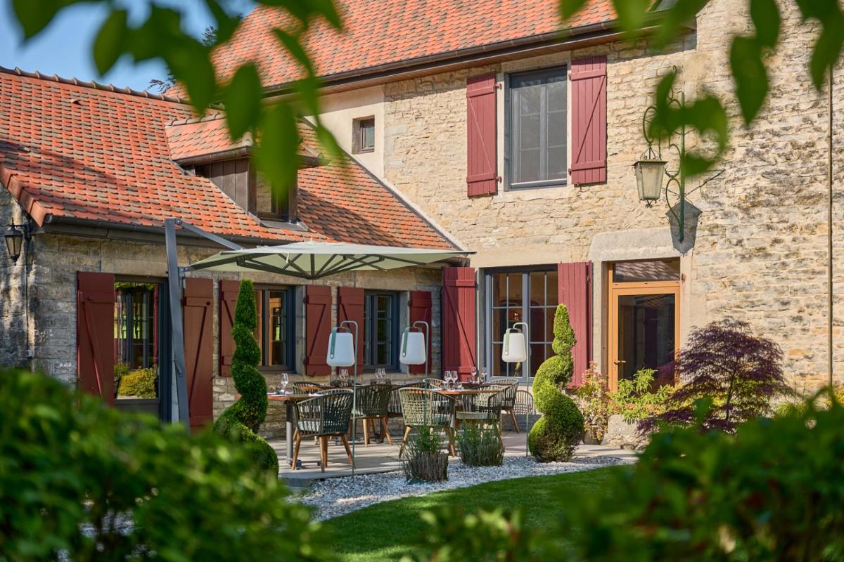 une terrasse avec une table et un parasol en face d'un bâtiment dans l'établissement Maison Zugno Hôtel & Spa, à Barretaine