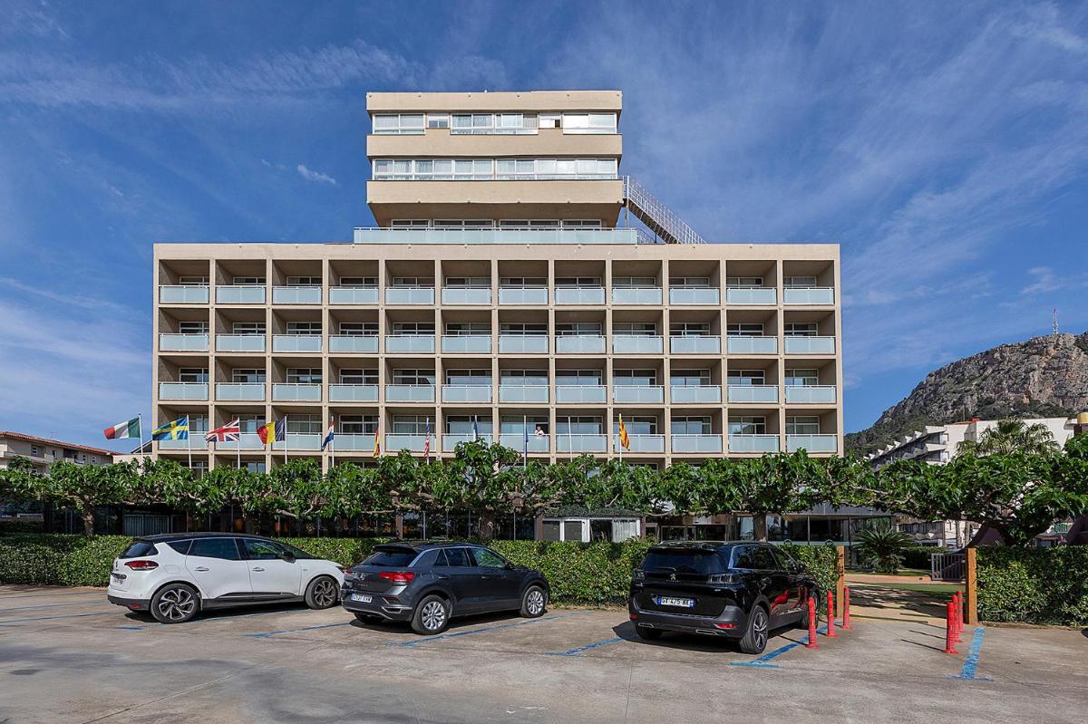 Un gran edificio con coches aparcados delante. en Hotel Panorama, en L'Estartit