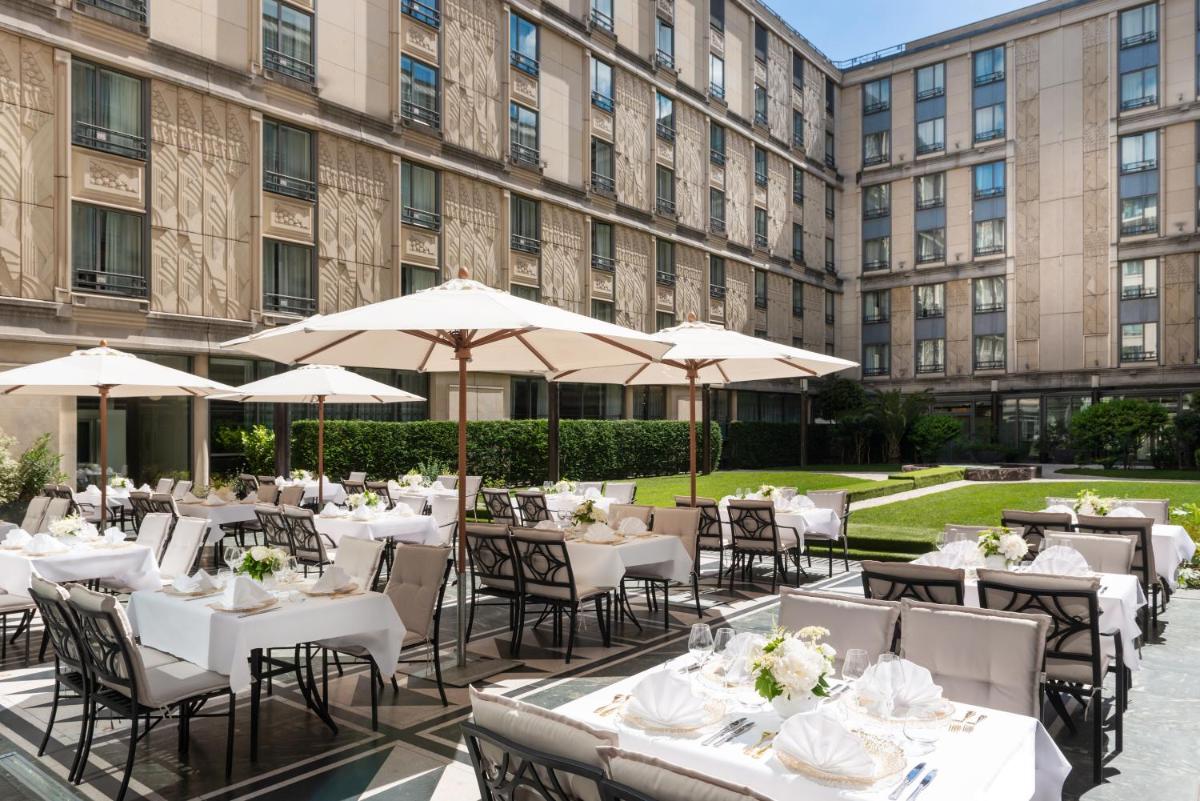 un restaurant avec des tables blanches et des parasols devant un bâtiment dans l'établissement L'Hôtel du Collectionneur Paris, à Paris