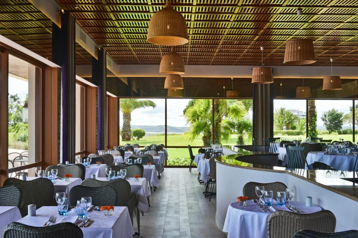 um restaurante com mesas e cadeiras brancas e grandes janelas em Pestana Alvor Praia Premium Beach & Golf Resort em Alvor
