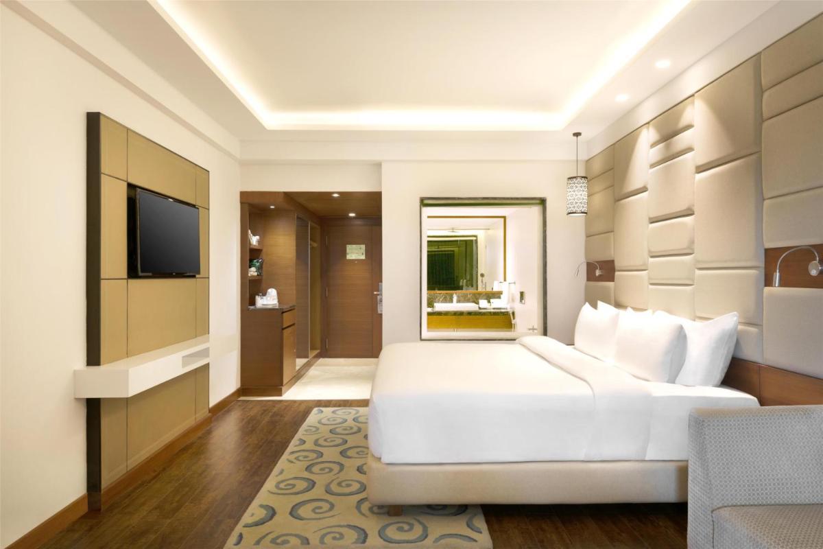 a bedroom with a white bed and a television at Radisson Jaipur City Center in Jaipur